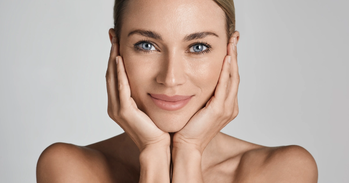 Close-up of a woman with hands framing her face, smiling slightly, for Skin Tightening in Centennial, CO.